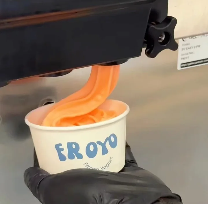 Peach frozen yogurt swirling from the machine into a Froyo cup