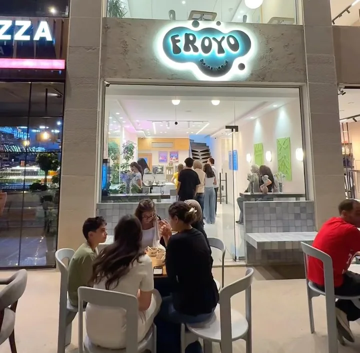 The Froyo storefront at night, glowing sign above, people sitting at the tables outside